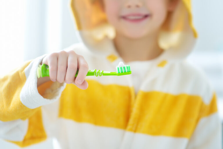 Kid in a yellow and white striped shirt smiles while showing his toothbrush with toothpaste